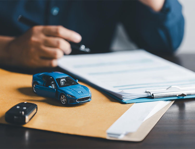 A person reviews a clipboard with documents, holding a pen. A blue toy car and a car key rest on a folder in the foreground, illustrating the car purchase or insurance process at Illinois Insurance Center.