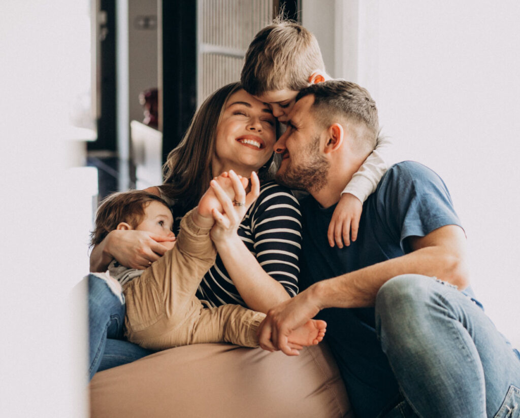 A joyful family of four sits closely together, laughing and hugging. The mother smiles while holding a young child, as the father embraces her and an older child—capturing the warmth and love Illinois Insurance Center seeks to protect.