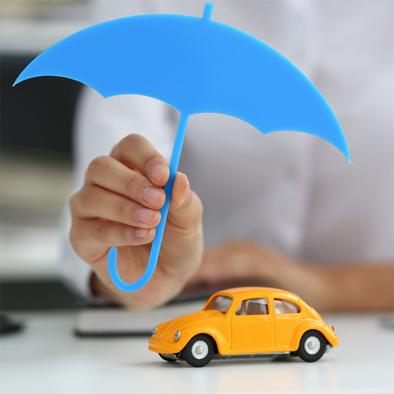 A person holds a blue umbrella cutout over a small yellow toy car, symbolizing protection and insurance—much like the coverage offered by Illinois Insurance Center.
