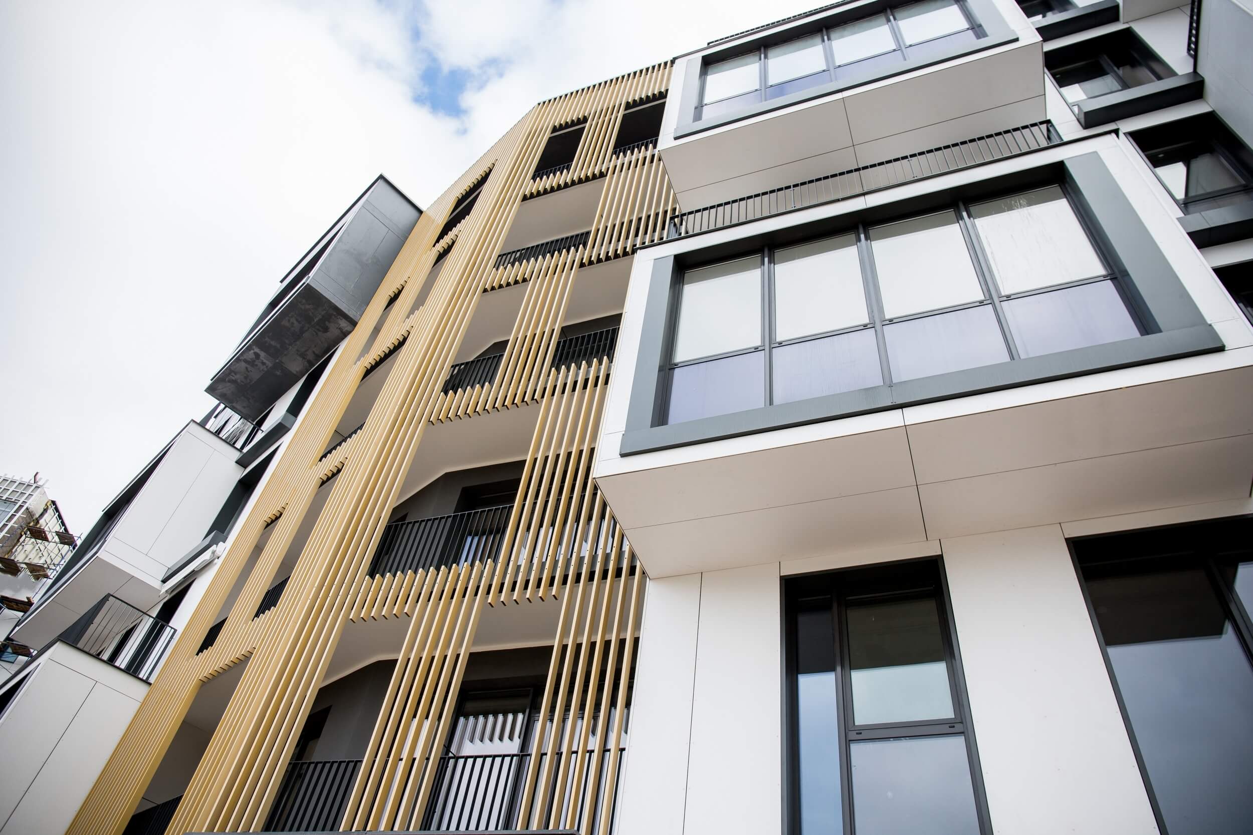 A low-angle view of a modern apartment building with large windows, white and beige facades, and vertical wooden slats, set against a partly cloudy sky—ideal for showcasing Commercial Property Insurance Illinois.