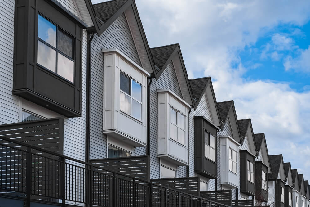 A row of modern townhouses with white and dark gray siding, triangular roofs, and black railings on the balconies in Addison IL, perfect for homeowners insurance peace of mind, set against a partly cloudy sky.