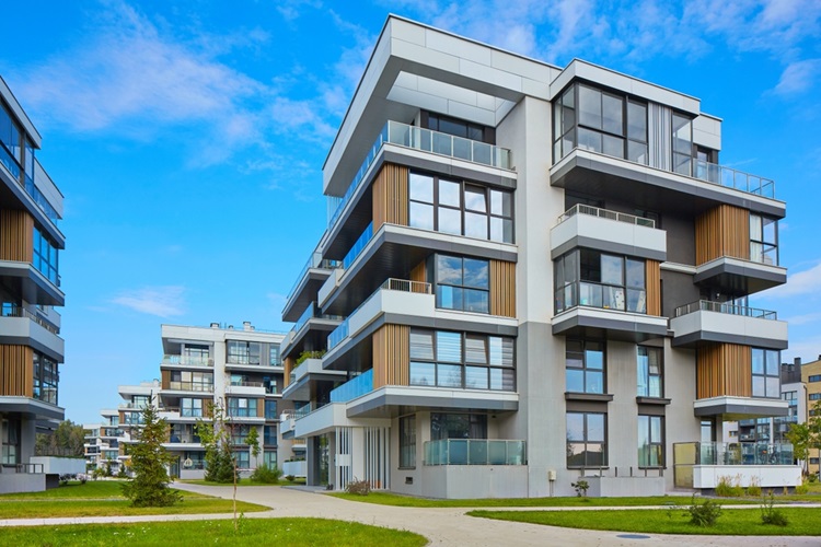 Modern apartment buildings with multiple balconies and large windows, set against a blue sky in Alsip IL. The buildings feature white and wood-paneled exteriors, surrounded by landscaped paths and green lawns—ideal for homeowners insurance coverage.