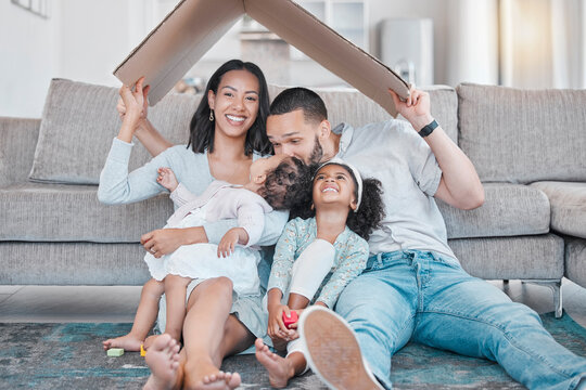 A family of four sits on the floor in front of a couch, smiling. The parents hold a cardboard piece above their heads like a roof—celebrating their Antioch IL home and the security that homeowners insurance brings.