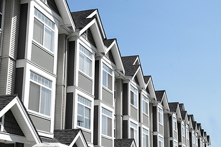 Row of modern gray and white townhouses with multiple windows and gabled roofs, shown from a low angle against a clear blue sky in Antioch IL—a perfect spot to consider comprehensive homeowners insurance.