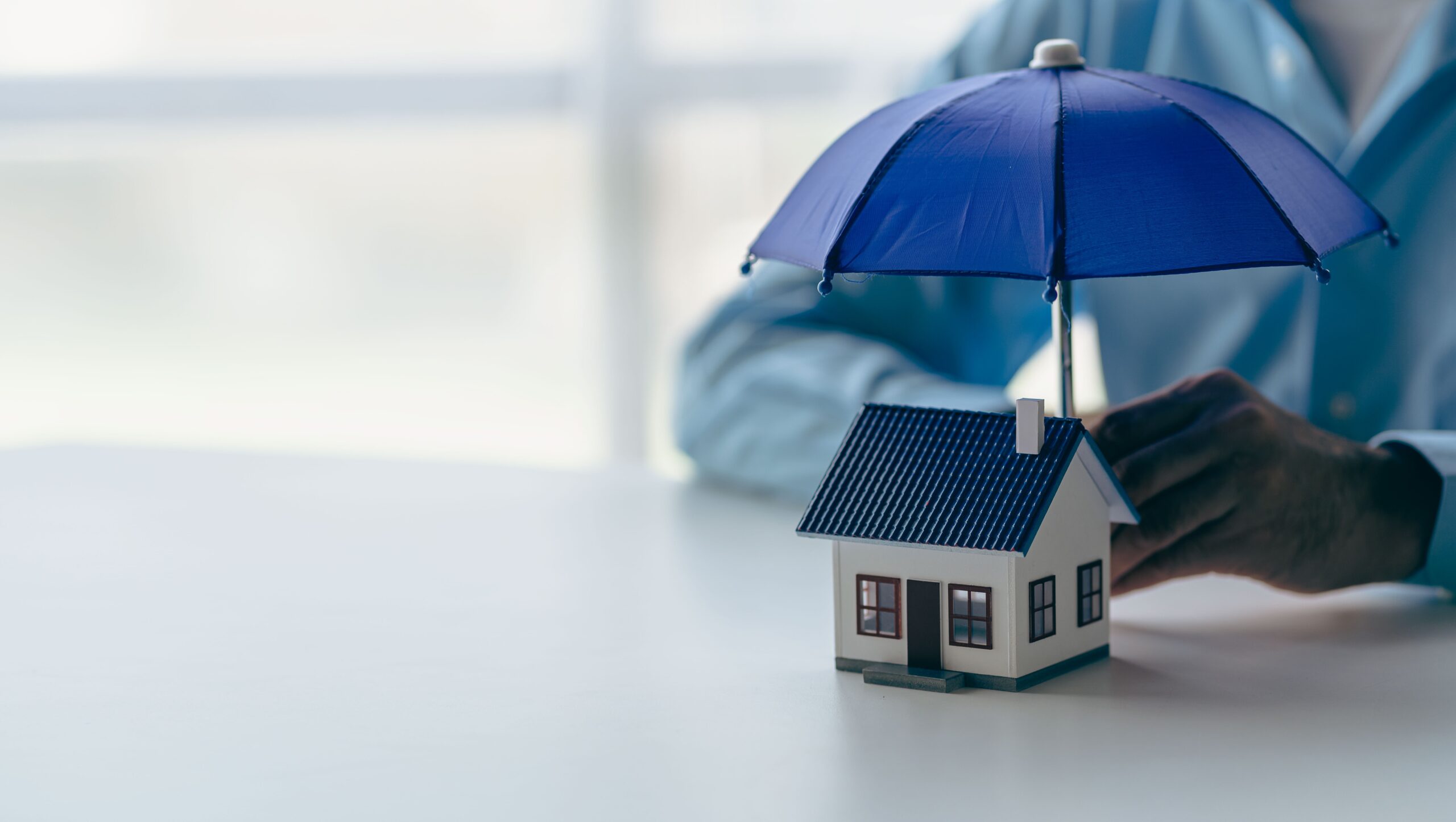 Home insurance protection concept showing miniature house covered by umbrella for homeowners