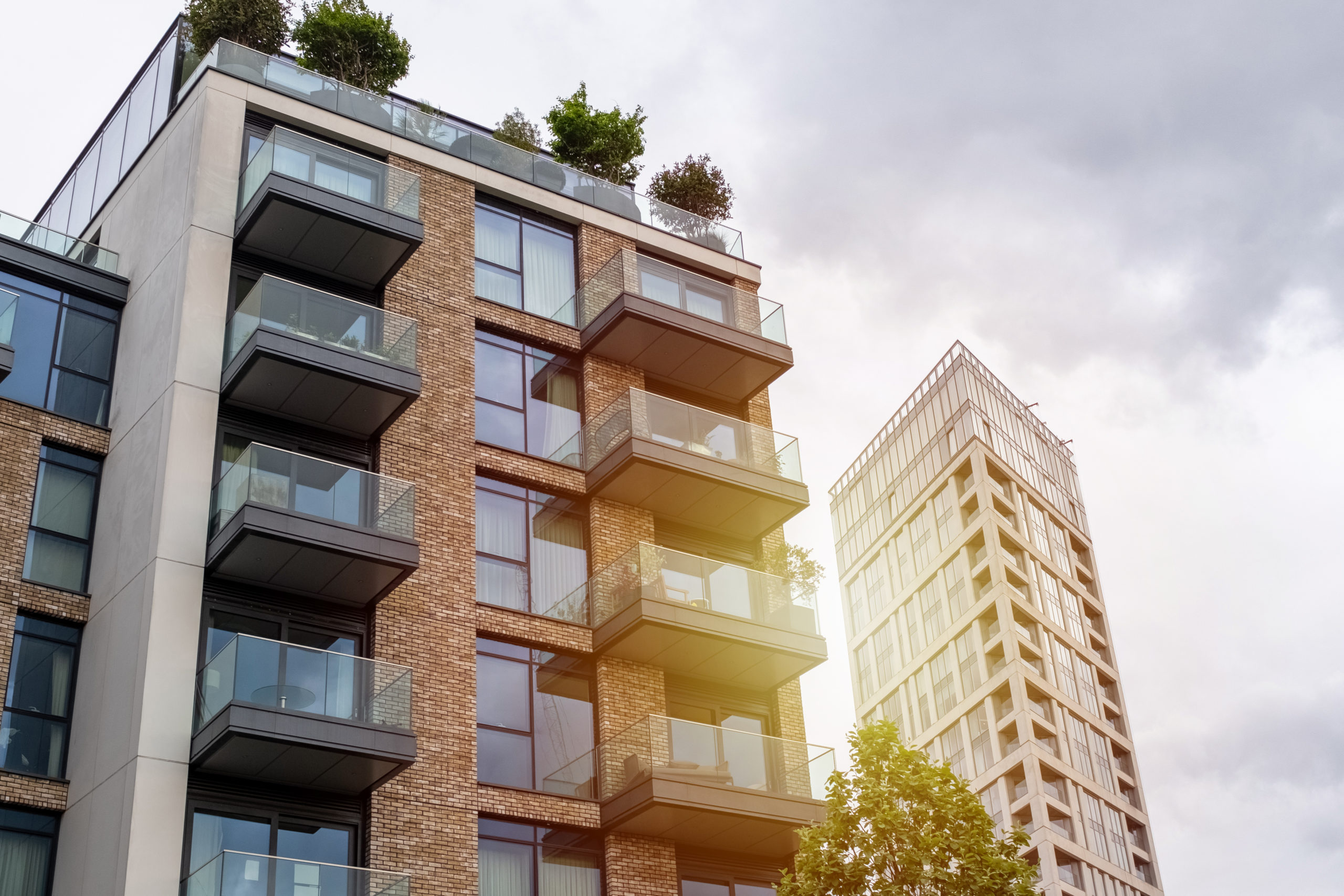 Modern apartment buildings with glass balconies and rooftop plants, including a brick facade in the foreground, stand tall under a cloudy sky in Belleville IL—an ideal spot where homeowners insurance can help protect your investment.