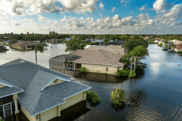 A residential neighborhood in Belvidere IL is flooded, with water covering streets and reaching up to house windows. Trees and lawns are partially submerged, under a mostly cloudy sky—highlighting the importance of homeowners insurance.