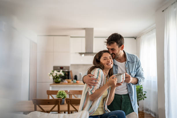 A man and woman stand in a bright kitchen in Belleville, IL, smiling and holding mugs. Relaxed and happy, they enjoy their modern space filled with plants and natural light—peace of mind thanks to homeowners insurance.
