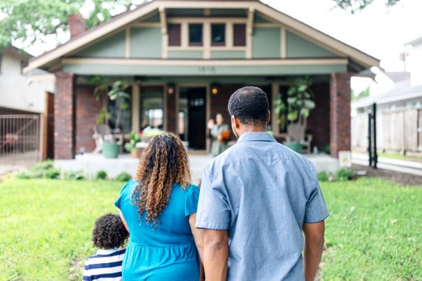A family of three stands on a lawn in Beach Park IL, facing their welcoming house with green siding, brick accents, and potted plants—an inviting scene that highlights the importance of homeowners insurance.
