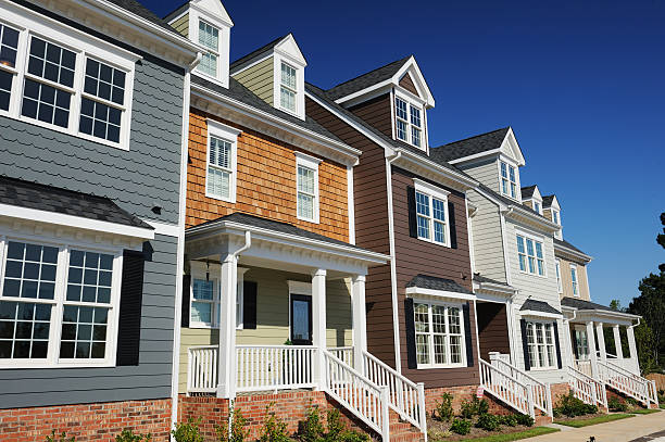 A row of modern, multi-story townhouses in Belvidere IL features varied colored siding, white trim, and covered front porches under a clear blue sky—ideal for those seeking stylish living with peace of mind from homeowners insurance.