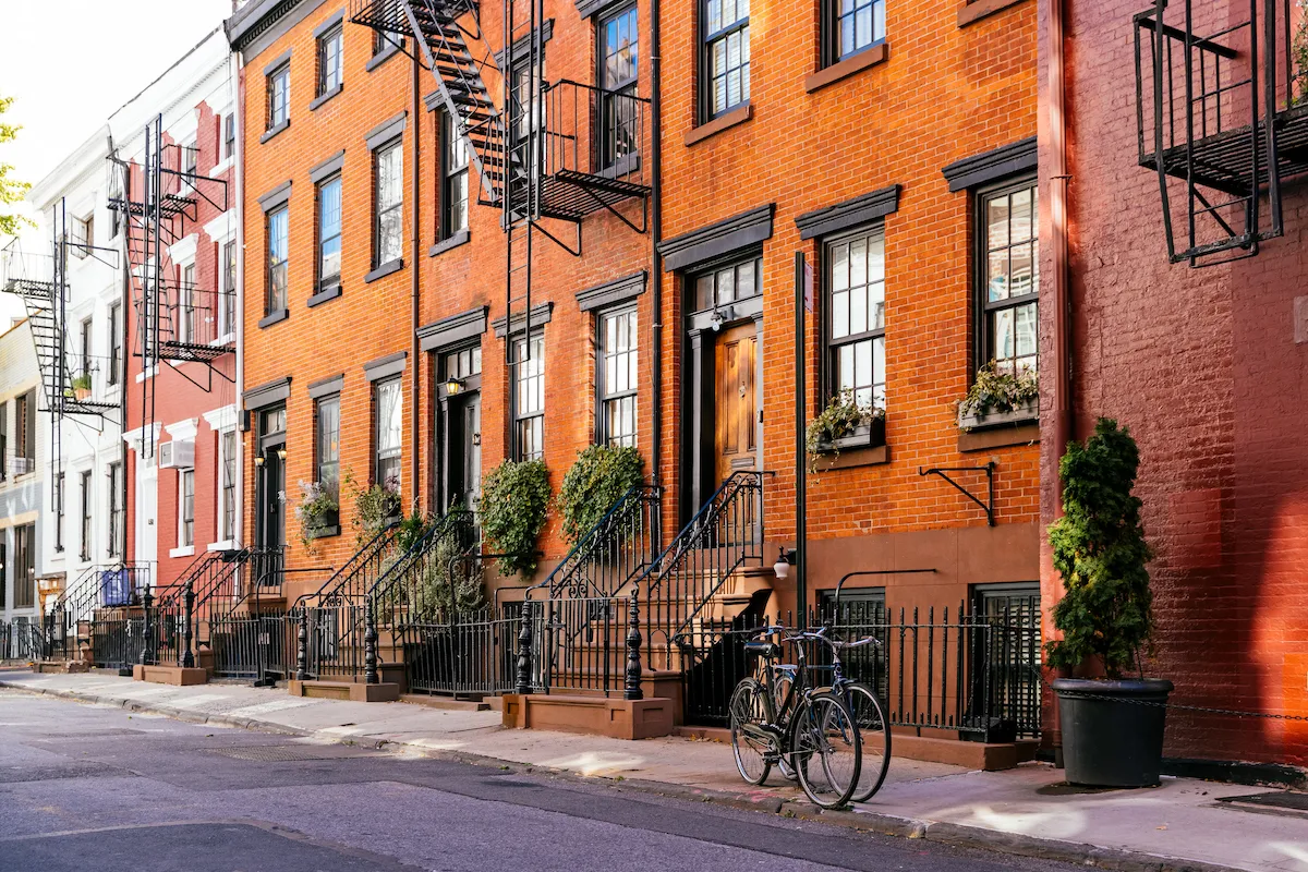 A row of red brick townhouses with black trim and iron railings lines a quiet city street in Bensenville IL. A bicycle rests by the sidewalk, stairs with potted plants lead to the doors, and homeowners insurance provides peace of mind above all.