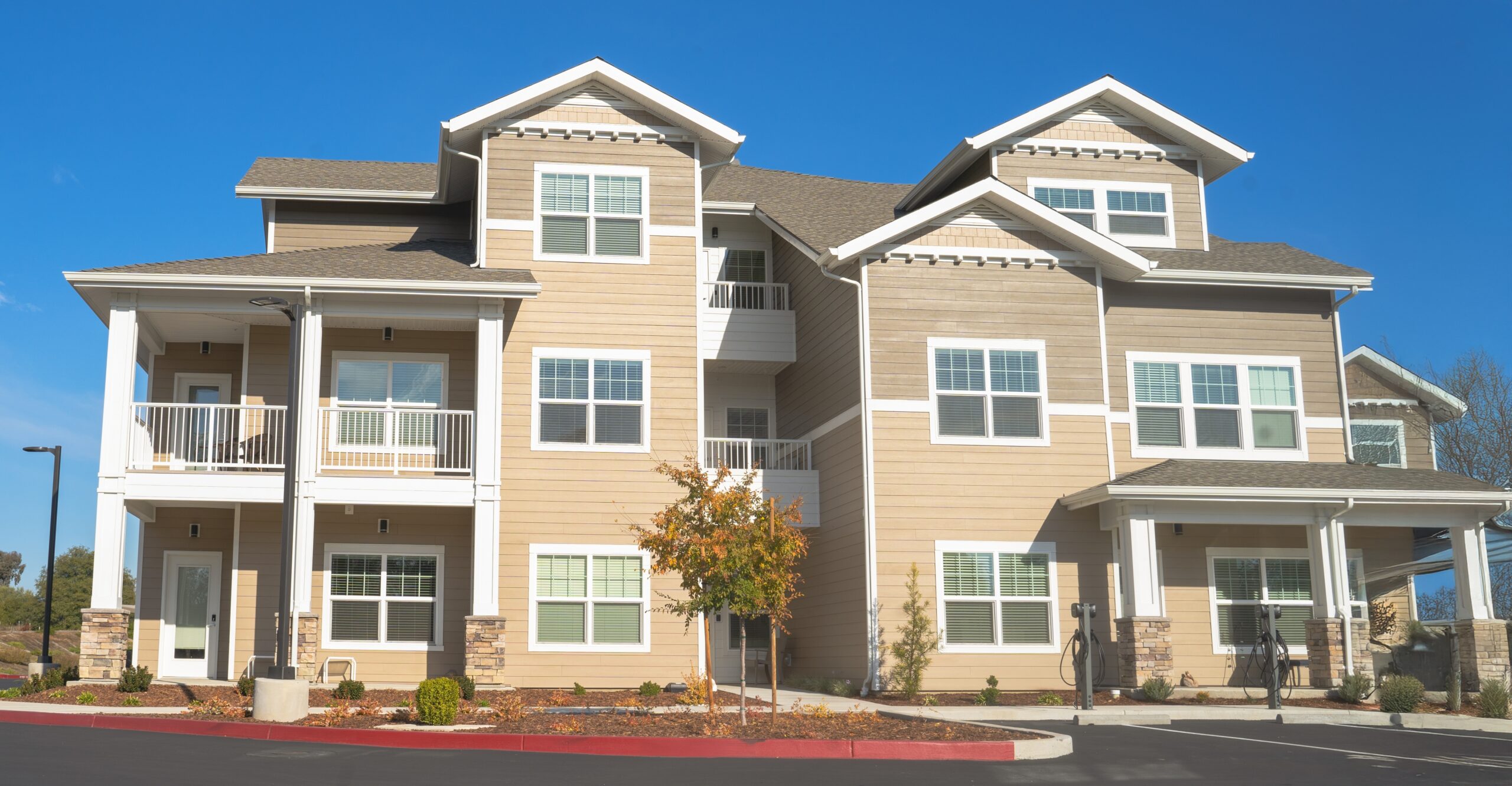 A modern three-story apartment building with beige siding, white trim, multiple balconies, and large windows is shown on a sunny day—perfect for those seeking style and peace of mind with homeowners insurance Berwyn coverage.