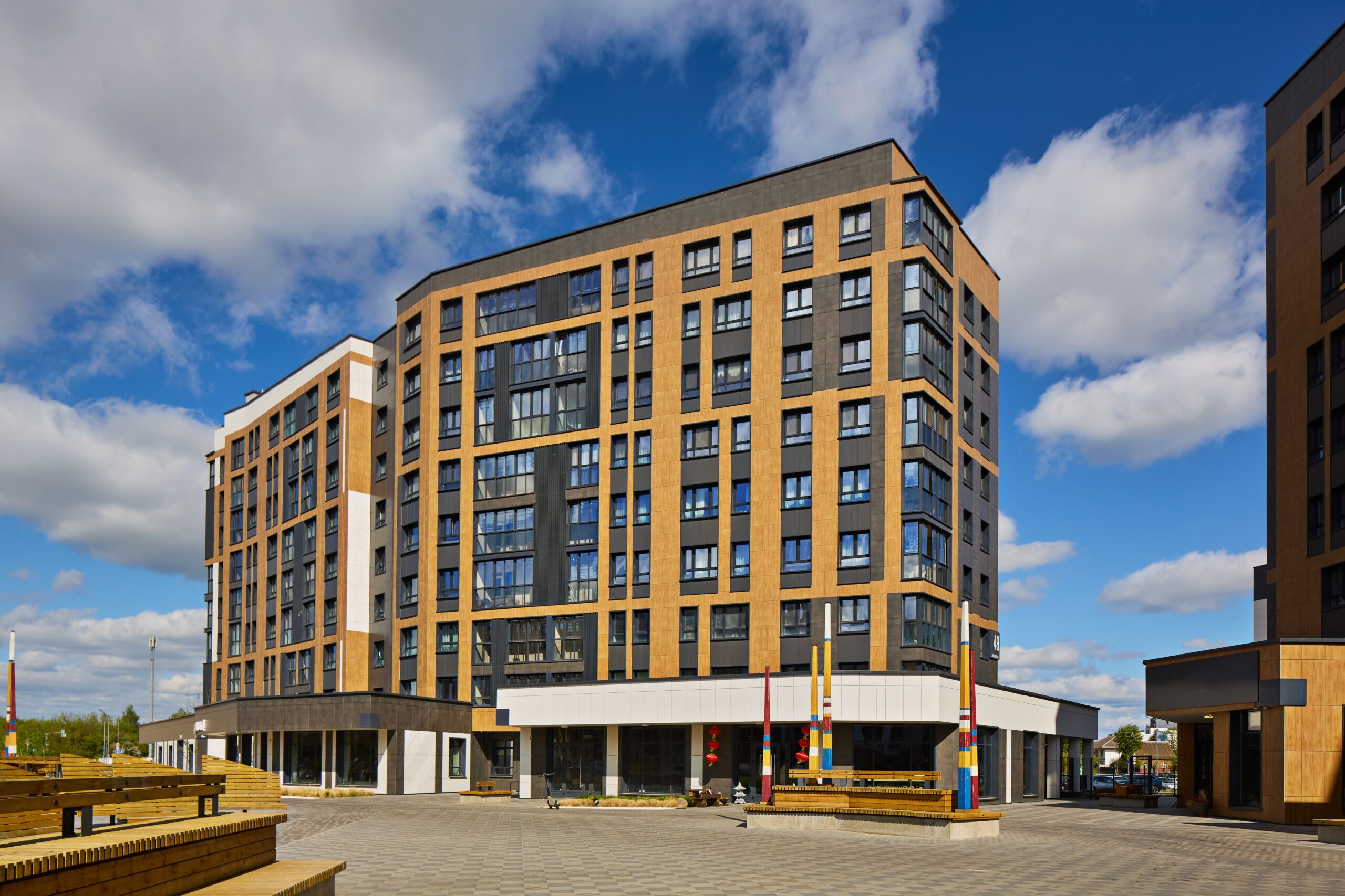 A modern mid-rise apartment building with large windows and a mix of beige and dark gray panels sits on a paved plaza—perfect for residents seeking comfort, style, and peace of mind with homeowners insurance in Brookfield IL.