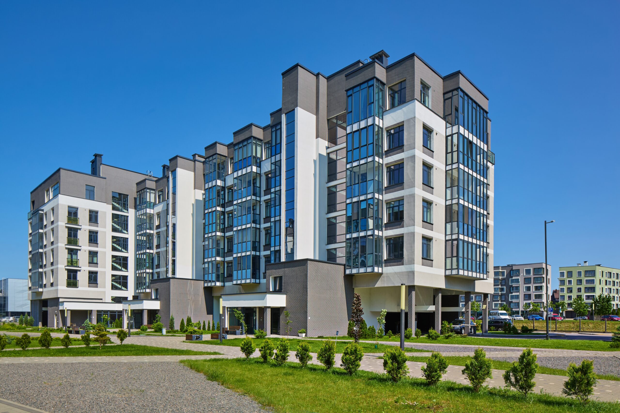 Modern multi-story apartment buildings with large glass windows stand under a clear blue sky. Pathways wind past green grass and shrubs, creating an inviting setting—perfect for those seeking peace of mind with Addison homeowners insurance.