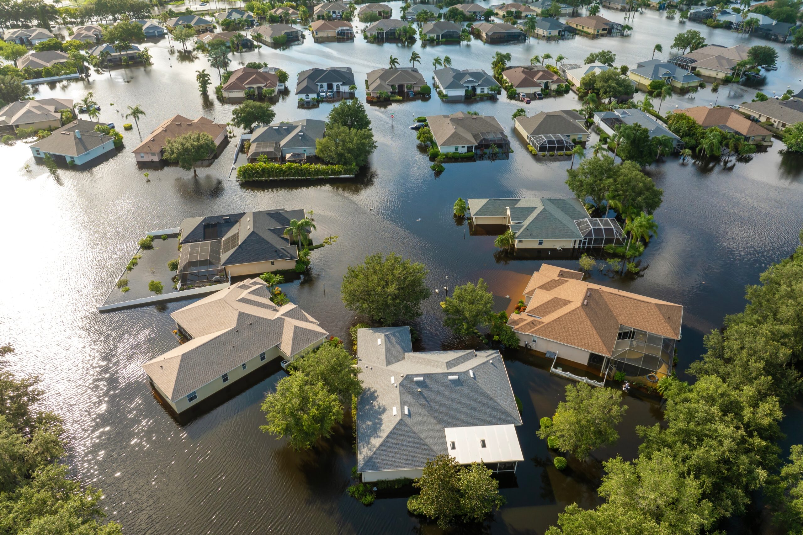 Aerial view of a residential neighborhood where floodwaters surround houses and trees, with streets and yards submerged, highlighting the importance of homeowners insurance Arlington in protecting against severe flooding in the area.